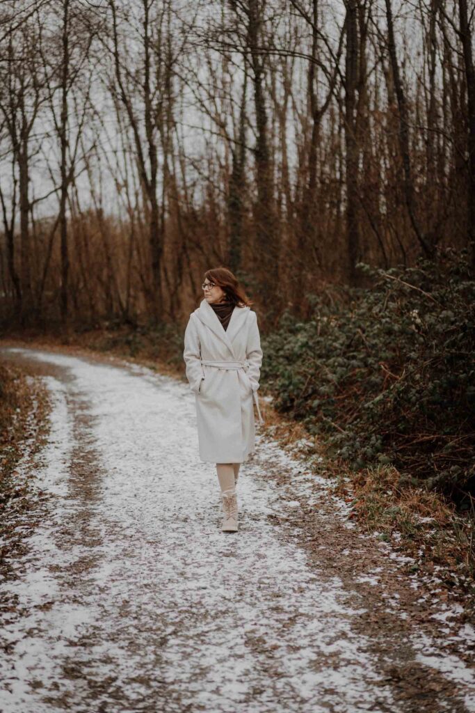 Simone Schuh in beigem Wintermantel spaziert durch Wald – vlygge Living für vegane Pionierinnen