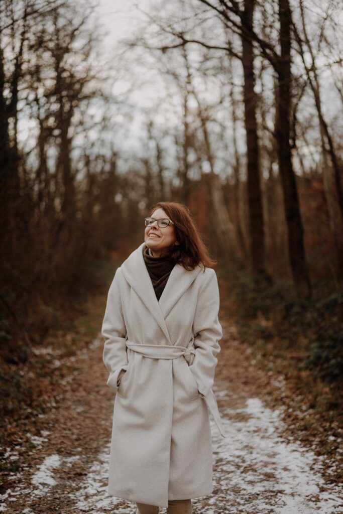 Simone Schuh von vlygge living spaziert durch verschneiten Wald und sieht in den Himmel